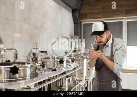 Professional brewer on his own craft alcohol production. Specialist, man wearing in workwear testing raw materials for manufacturing. Concept of open business, eco product, craft brewery, factory. Stock Photo