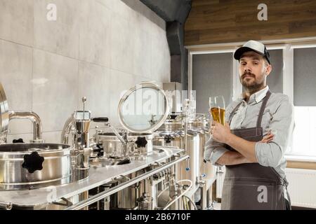 Professional brewer on his own craft alcohol production. Specialist, man wearing in workwear testing, trying product on its taste, color and smell. Concept of open business, eco product, craft brewery. Stock Photo