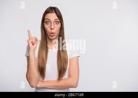 Photo of pretty lady nave awesome idea hold index finger raised wear specs and t-shirt isolated white background Stock Photo