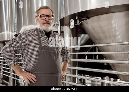 Professional brewer on his own craft alcohol production. Specialist, senior man in workwear posing confident. Concept of open business, eco product, craft brewery, factory, manufactory, start up. Stock Photo