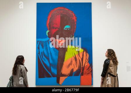 London, UK.  10 March 2020. Staff members pose next to 'Ladies and Gentlemen (Wilhelmina Ross)', 1975, (images of New York black and latino drag queens and trans women) by Andy Warhol. Preview of 'Andy Warhol', a retrospective of over 100 works by one of the most recognisable artists of the late 20th century.  The exhibition runs 12 March to 6 September 2020 at Tate Modern. Credit: Stephen Chung / Alamy Live News Stock Photo