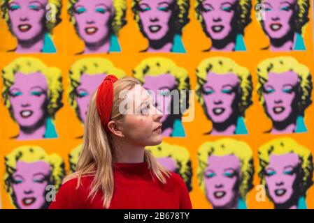 London, UK.  10 March 2020. A staff member poses next to 'Marilyn Diptych', 1962, by Andy Warhol. Preview of 'Andy Warhol', a retrospective of over 100 works by one of the most recognisable artists of the late 20th century.  The exhibition runs 12 March to 6 September 2020 at Tate Modern. Credit: Stephen Chung / Alamy Live News Stock Photo