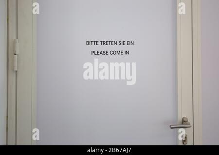 a white door with the inscription 'Please come in' in german and english Stock Photo