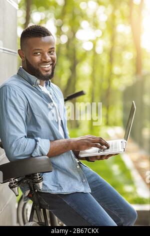 Handsome black man leaning on his bike and using laptop Stock Photo