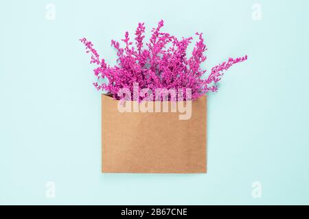 Bright purple or violet flowers in craft brown envelope with copy space isolated on light blue background. Trendy banner for Valentines Day or Interna Stock Photo