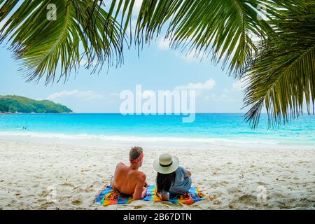 Tropical white beach at Praslin island Seychelles, happy Young couple man and woman during vacation Holiday at the beach relaxing under a palm tree Stock Photo