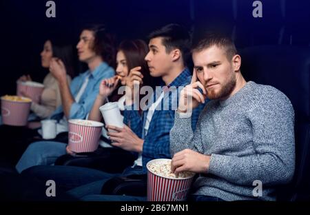 Dull movie. Bored man with company of people in cinema Stock Photo