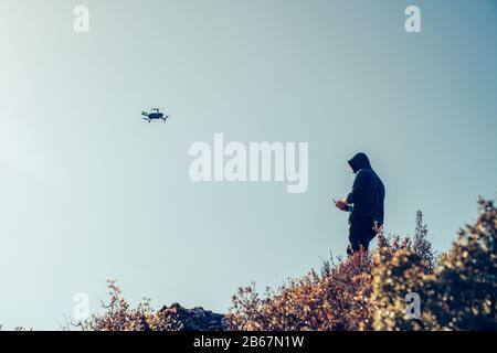 A silhouette of a Quadrocopter drone and the pilot is controling it, with the camera against the blue sky Stock Photo