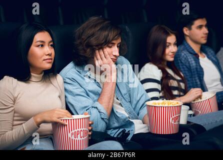 Handsome young man feeling bored while watching film in cinema Stock Photo