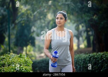 Fit woman with dumbbell shape water bottle at park Stock Photo