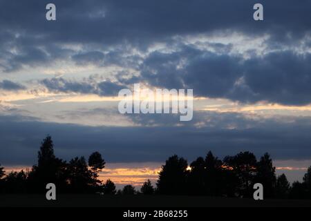 Dramatic sunset clouds dark clouds and orange sun with dark trees silhouette. Vibrant colors picturesque Stock Photo