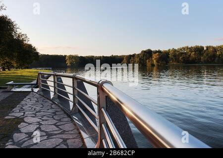 City park in Minsk at sunset. Tree on river bank with metal contraction bridge pier, nice evening mood Stock Photo