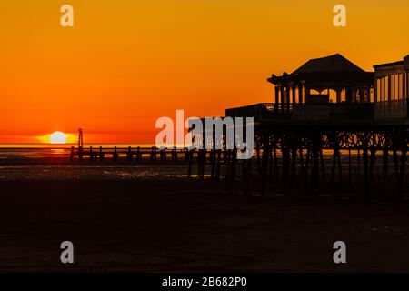 a golden sky as the sun sets behind the silhouette of the Victorian pier at St Annes on Sea in Lancashire england Stock Photo