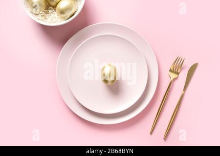 Easter table setting with golden eggs in bowl on pink table. Elegance dinner. Top view. Stock Photo