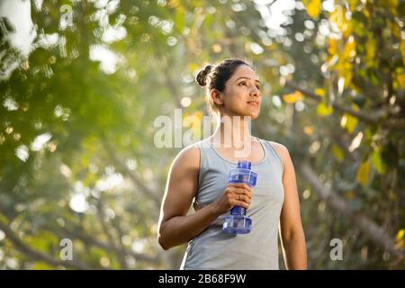 Fit woman with dumbbell shape water bottle at park Stock Photo