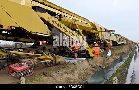 10 March 2020, Schleswig-Holstein, Südermarsch: With the help of a track-laying train, the ballast bed on the Marschbahn line between Husum and Friedrichstadt is being rehabilitated and the subgrade improved. This year, Deutsche Bahn intends to renew a total of around 52 kilometres of track and several points on the Marschbahn line between Hamburg and Westerland on Sylt. The investment sum amounts to 50.7 million euros. Photo: Carsten Rehder/dpa Stock Photo