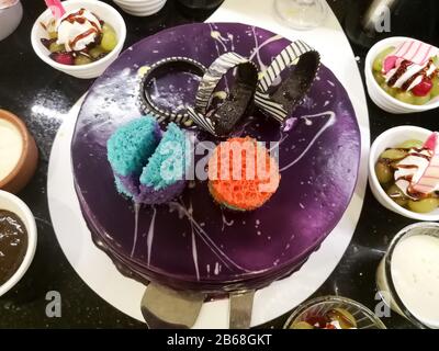Decorated dark purple cake surrounded by dessserts Stock Photo