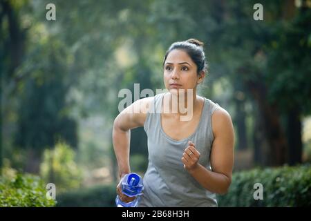 Fit woman with dumbbell shape water bottle at park Stock Photo