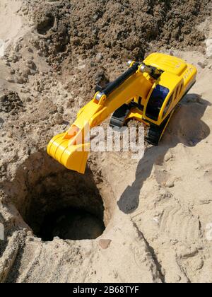 Plastic toy excavator prepared for digging hole on the sandy beach Stock Photo