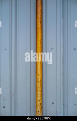 Orange gutter drain pipe against corrugated metal warehouse wall, close up Stock Photo