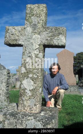 man kneeling by old stone cross in graveyard Stock Photo