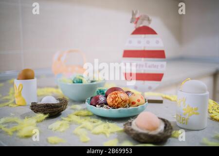 Painted eggs with Easter decoration on counter. Colored eggs in bowl with egg in nest, feathers, bowl and wooden Easter decoration on kitchen countert Stock Photo