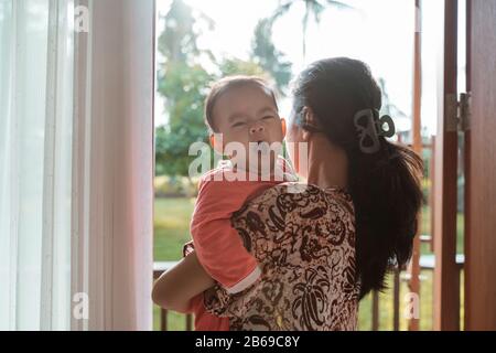 mother holding a sleepy baby girl while standing in front of the door