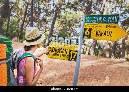13 SEPTEMBER 2017, TURKEY, LYCIAN WAY: Woman hiker with backpack looking at the Lycian Way route sign pointing at Adrasan and Gelidonya lighthouse Stock Photo