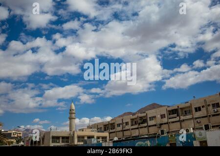 AQABA, JORDAN - JANUARY 31, 2020: Beautiful winter puffy white clouds moving in sky over the famous city. Red Sea gulf, Hashemite Kingdom of Jordan. Street view with mosque and residential buildings Stock Photo