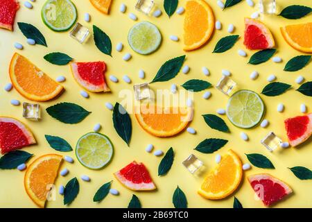 Pattern of citrus lemon, lime, orange and grapefruit slices, mint herbs, cubes of ice and fresh pills on yellow background. Top view. Minimal design background. Stock Photo