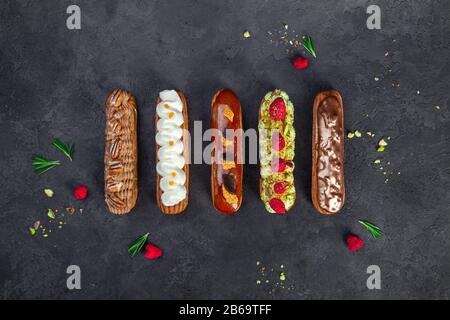 Set of tasty french sweet and colorful dessert Eclair with icing, cream, fresh berries and decor on dark textured background, homemade profiteroles Stock Photo