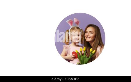 Easter card! Mother and daughter with yellow flowers tulip and greeting card with heart. Cute little child girl is wearing bunny ears. Round hole in w Stock Photo