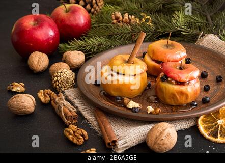 Baked apples on brown plate with holiday Christmas decoration with Christmas tree branch, cones, cinnamon, walnuts and red apple. Stock Photo