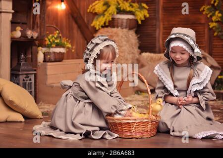 Two happy little sisters in retro outfits play with ducklings. Country style. Easter Stock Photo