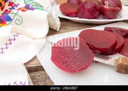 Cutting beetroot on white chopping board over on old wooden table. Rustic style Stock Photo