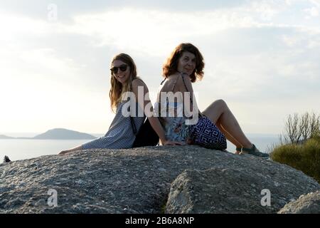 Mother and daughter sit back to back atop a large granite boulder on Wilsons Promontory Stock Photo