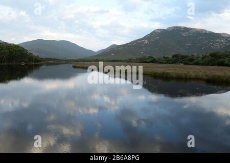 Early morning sky with Mt Ramsay (left) and Mt Mcalister reflected in the glassy waters of Tidal River Stock Photo