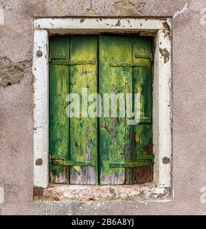 Old green weathered wooden shutters with a white window frame, Murano, near Venice, Italy Stock Photo