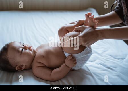 mother stretch her baby feet on the bed giving massage Stock Photo