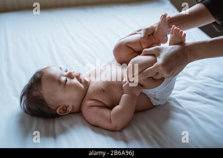 mother holds the feet of a baby child lying in bed giving massage Stock Photo