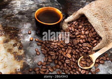 Roasted coffee beans in small sack and cup of coffee over on metal surface. Rustic country style Stock Photo