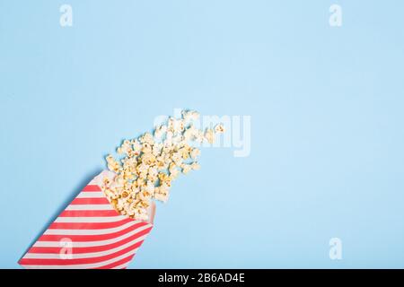 Spread popcorn on blue background in red striped popcorn pack. Free copy space. Cinema Entertainment  Stock Photo