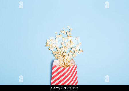 Spread popcorn on blue background in red striped popcorn pack. Free copy space. Cinema Entertainment  Stock Photo