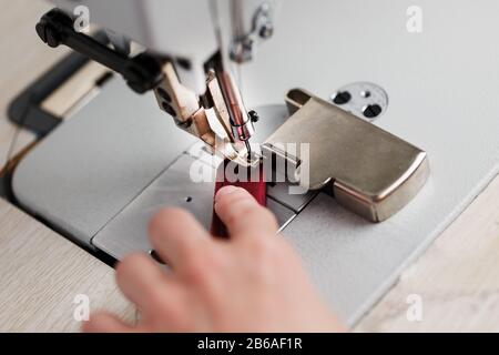 The hands of a master and the needle of a leather product sewing on a sewing machine. Manual work, business. Close up Stock Photo