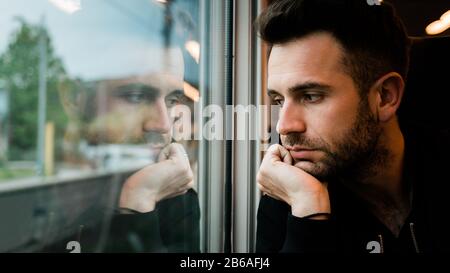 Young bearded man traveling by train in late afternoon Stock Photo
