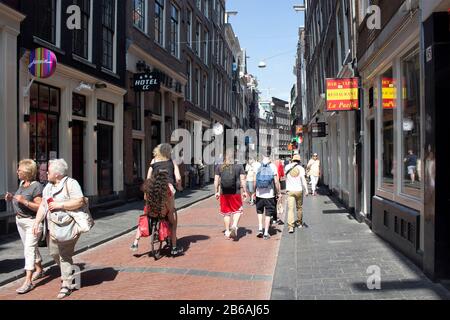 View of people walking on Warmoesstraat street in Amsterdam. It is one of the oldest streets with many cafes, restaurants and shops. It is a sunny sum Stock Photo