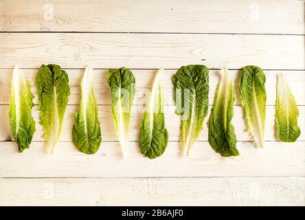 Raw of fresh organic romain lettuce salad leaves from big to small on white wooden backgruond. Top view. View from above. Copy space Stock Photo