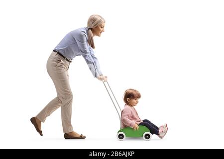 Mother pushing toddler girl inside a wooden toy cart isolated on white background Stock Photo