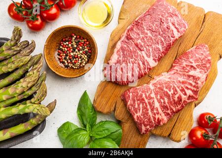 Raw Steak with green asparagus on white background, top view Stock Photo