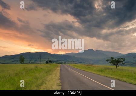 A road leading towards Champagne Castle mountains, at sunset in central Drakensberg, near Winterton, KwaZulu-Natal, South Africa Stock Photo